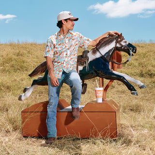 Man sitting on a mechanical horse in an open field with a clear blue sky.
