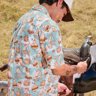 Man wearing a patterned shirt standing next to a motorcycle in an outdoor setting