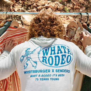 Person wearing a 'Whata Rodeo' shirt with a graphic design, standing in front of a rack of clothes.