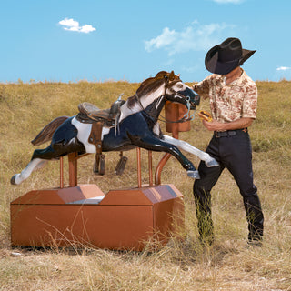Man in cowboy hat interacting with a mechanical horse in an open field