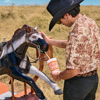 Man in cowboy hat interacting with a toy horse in an outdoor setting.