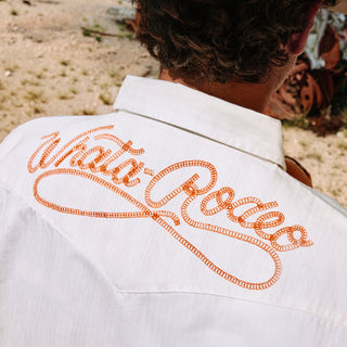 White shirt with orange embroidered text on a desert background