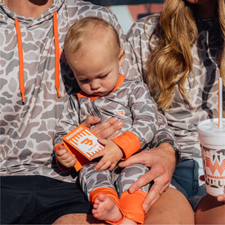 Baby in camo onesie sitting on an adult's lap, holding a Whataburger french fry box with a Whataburger cup nearby.