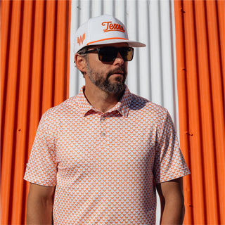 Bearded man wearing a white hat with "Texas" embroidered and an orange patterned polo shirt featuring mini Whataburger logos.