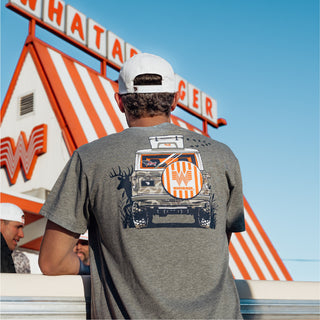 Man wearing a gray t-shirt with a graphic of a truck, deer silhouette, and Whataburger spare tire in front of a Whataburger building.