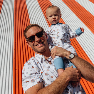 Man in the printed button-up holding a baby wearing a matching Whataburger-themed onesie.