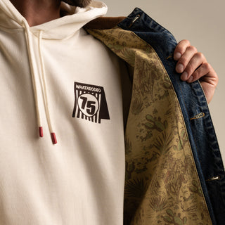 Person wearing a white hoodie with a logo, holding a patterned jacket.