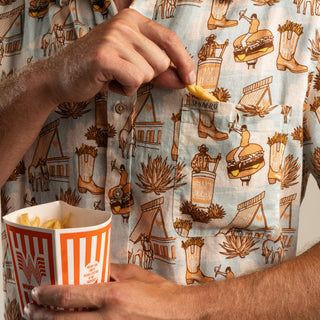 Person eating fries from a container with a patterned shirt featuring cowboy and desert-themed designs.