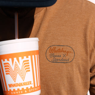Person wearing a brown sweatshirt with a Whataburger logo, holding a Whataburger cup.