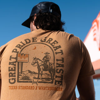 Person wearing a brown t-shirt with a graphic and text, standing against a clear blue sky.