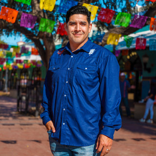 Man wearing a blue shirt with a logo in an outdoor setting with colorful flags and people in the background