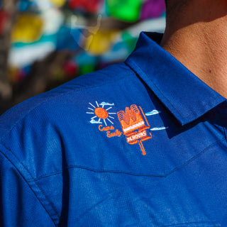 Blue shirt with an embroidered logo on the chest against a colorful blurred background