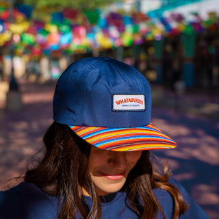 Person wearing a blue cap with a Whataburger logo and a colorful striped visor, blurred background
