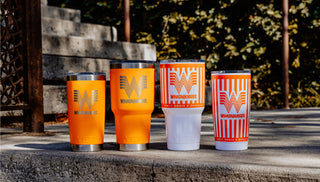 Four orange and white YETI tumblers with a Whataburger logo on a stone surface outdoors.