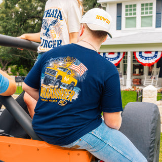 Man sitting on edge of orange truck wearing Howdy Hat and Navy Truck tee