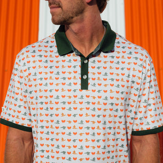 A man wearing a white short-sleeve polo shirt with a dark green collar and sleeve cuffs, featuring an all-over repeating pattern of small Whataburger Flying W logos and blue and gold mallards. The shirt has a three-button placket.