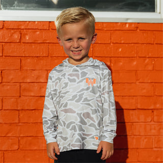 Child smiling in front of orange brick building wearing a Youth White Camo Performance Hoodie.