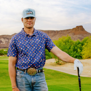 Man on a golf course wearing a patterned shirt, jeans, and a cap, holding a golf club.