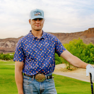 Man on a golf course wearing a patterned shirt, jeans, and a cap, holding a golf club.