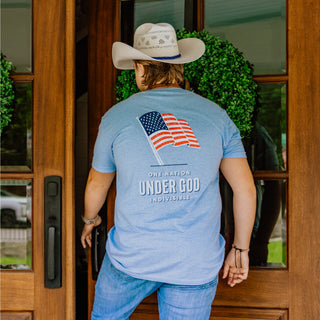 Person wearing a blue t-shirt with an American flag, standing in front of a wooden door.