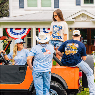 Group of people standing around an orange vehicle with a house and American flag in the background