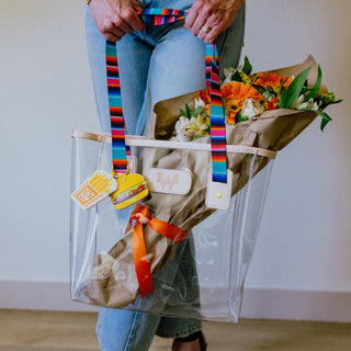 Clear Jon Hart Serape Tote holding flowers and Burger and Fries Bag Charm set, against a plain background