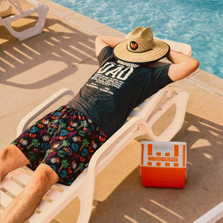 Man lounging by a pool with a Whataburger branded hat and WhataDad Ingredient tee with hat over face.