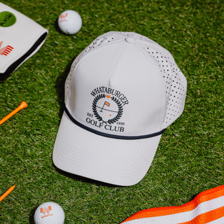 White cap with 'Whataburger Golf Club' logo on a grassy surface with golf balls and tees.