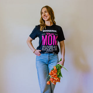 Woman wearing a black WhataMom Ingredient tee, holding flowers against a plain background